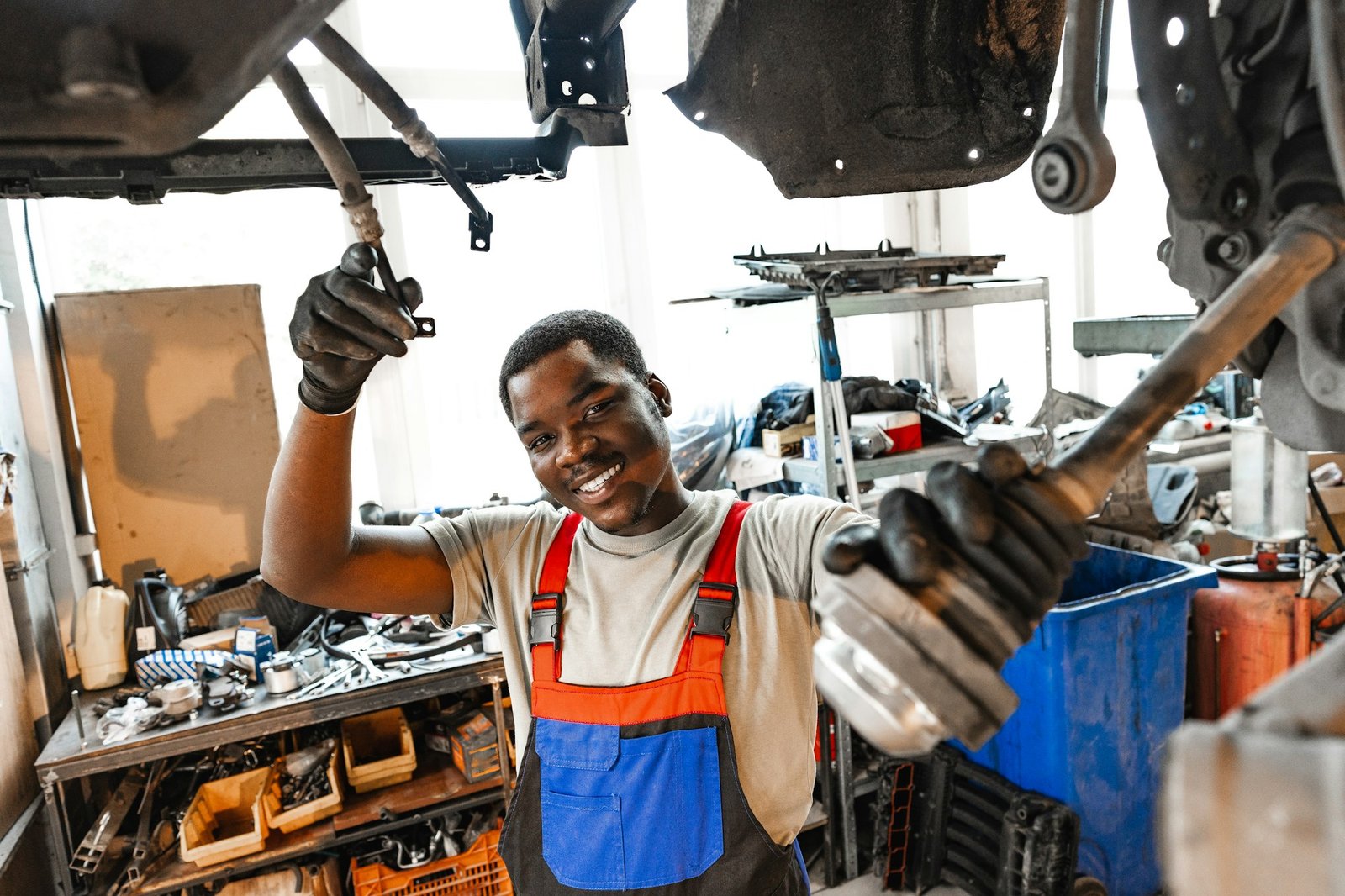 Young African mechanic in uniform working under the car in car service center